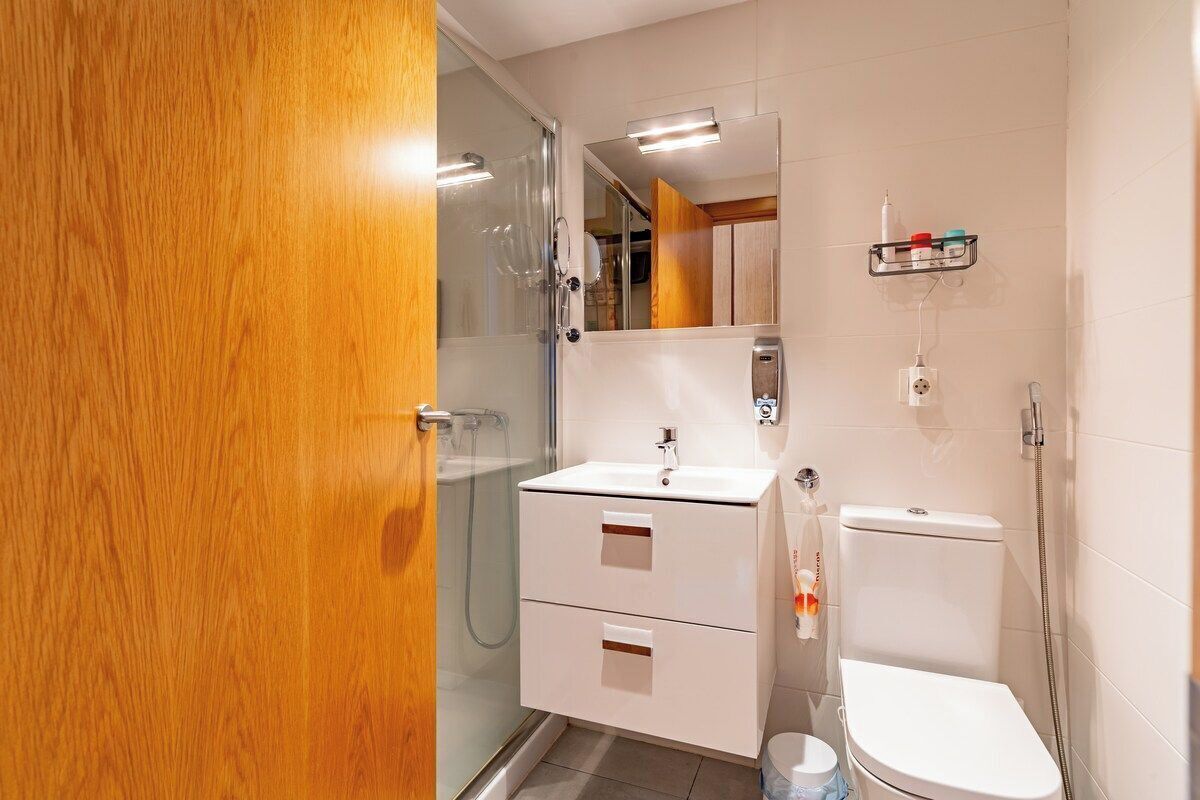 Une salle de bain avec une douche à parois de verre, un lavabo blanc, des toilettes et un miroir au-dessus du lavabo.