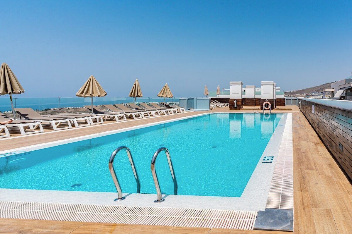 A pool with lounge chairs and umbrellas, a lifebuoy, and a view of the sea.