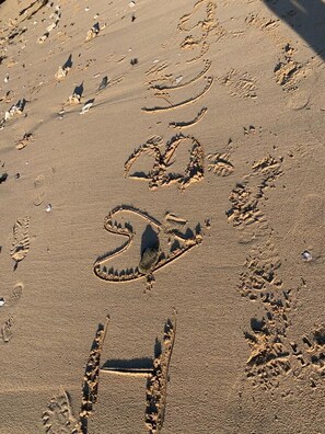 Ein sandiger Strand mit Fußabdrücken und einem wellenartigen Muster.