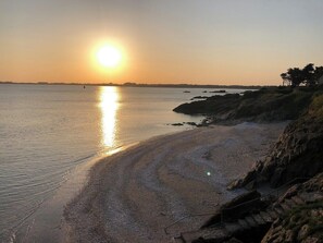 Ranta, jossa on näkyvissä auringonlasku, tyyni vesi ja kivikkoista maastoa.