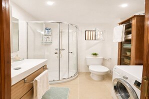 A bathroom with a shower, toilet, sink, and a washing machine. - Cozy apartment on the sea shore (Costa de la Calma)
