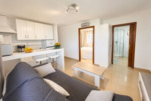 A modern, well-lit room with a sofa, a small dining table, and a kitchen area with cabinets and a fruit bowl. - Cozy apartment on the sea shore (Costa de la Calma)