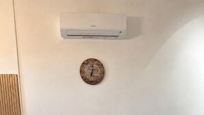 Ein Essbereich mit einem Holztisch, zwei weißen Stühlen, einer Klimaanlage und einer Uhr an der Wand.