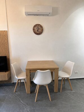 Ein Essbereich mit einem Holztisch, zwei weißen Stühlen, einer Klimaanlage und einer Uhr an der Wand.