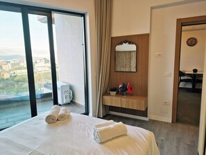 Ein Hotelzimmer mit Bett, Schminktisch mit Spiegel, Blick auf die Stadt und Schreibtisch mit Stühlen.