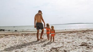 Una spiaggia con una persona e due bambini che camminano sulla sabbia.