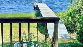 Une terrasse en bois agrémentée de plantes en pot, donnant sur un lac avec une jetée qui s’avance dans l’eau.