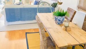 Zona pranzo con tavolo in legno e sedie in vimini, un vaso con decorazioni blu e bianche e una lanterna a sospensione.