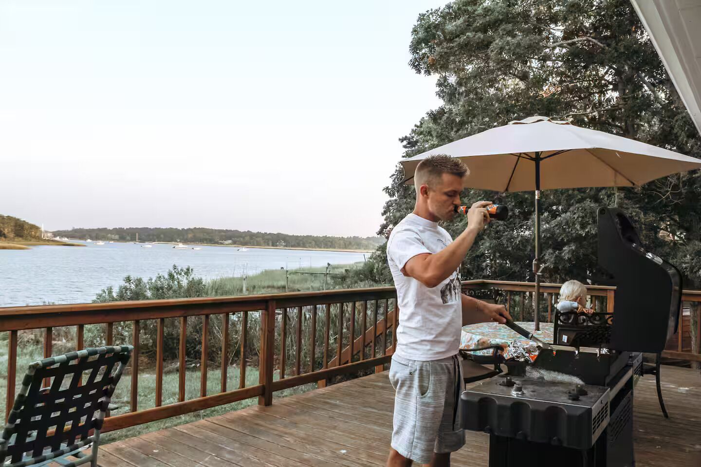Une personne qui fait griller des aliments sur une terrasse en bois, avec vue sur un lac et des bateaux.