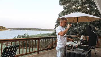 Une personne qui fait griller des aliments sur une terrasse en bois, avec vue sur un lac et des bateaux.