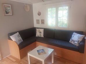Een woonkamer met een donkergrijze bank, een witte salontafel en een raam met uitzicht op groen.