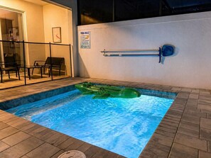 Una pequeña piscina interior con un flotador hinchable verde, una silla junto a la piscina y un cartel con las normas de la piscina.
