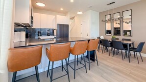 A modern kitchen with a central island, bar stools, and a dining area with a table and chairs. - 4BR Private Pool Home with Lake View Near Disney | Sleeps 10 (Clermont)