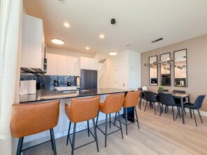 A modern kitchen with a central island, bar stools, and a dining area with a table and chairs. - 4BR Private Pool Home with Lake View Near Disney | Sleeps 10 (Clermont)