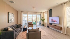 A modern living room with a sofa, armchairs, a coffee table, a TV, and a balcony with a view. - 4BR Private Pool Home with Lake View Near Disney | Sleeps 10 (Clermont)