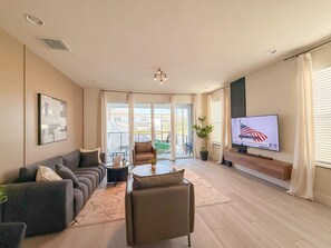 A modern living room with a sofa, armchairs, a coffee table, a TV, and a balcony with a view. - 4BR Private Pool Home with Lake View Near Disney | Sleeps 10 (Clermont)