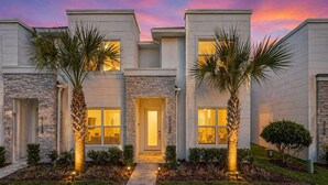 A modern two-story house with a stone facade, a central entrance, and palm trees. - 4BR Private Pool Home with Lake View Near Disney | Sleeps 10 (Clermont)