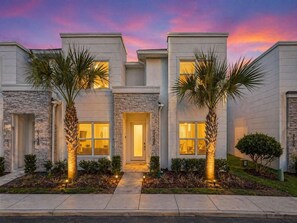 A modern two-story house with a stone facade, a central entrance, and palm trees. - 4BR Private Pool Home with Lake View Near Disney | Sleeps 10 (Clermont)