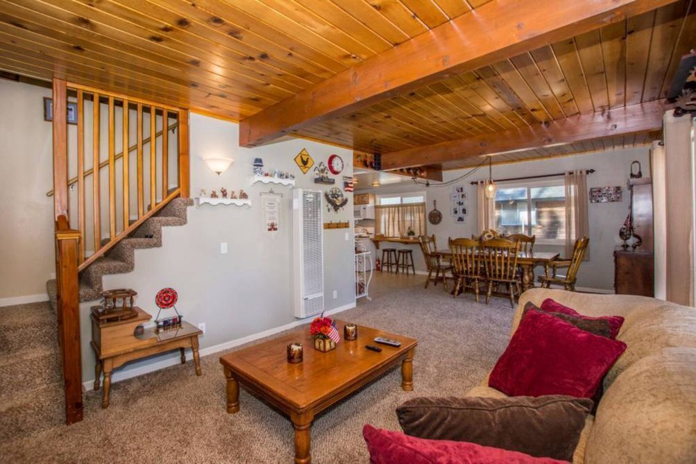 A cozy living room with a wooden staircase, a dining area, and a kitchen in the background.