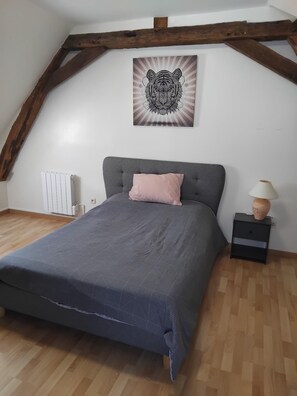 Een slaapkamer met een grijs bed, een roze kussen, een houten hoofdbord, een radiator, een nachtkastje met een lamp en een wanddecoratie met tijgers.