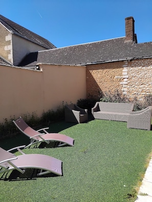 Ein Garten mit Kunstgrasanlage, zwei Korbsessel und einer Steinmauer.