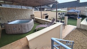 Un pati amb un banyera d'hidromassatge, una barbacoa, una zona de seients coberta i una paret de pedra.