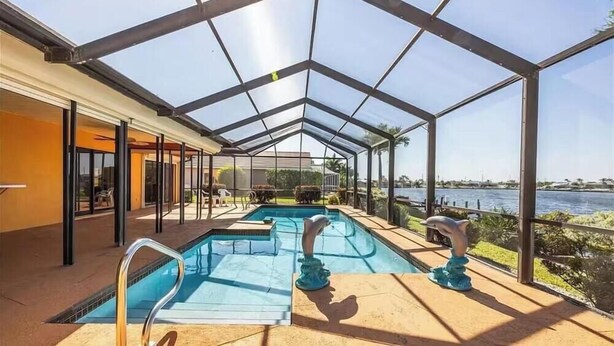 A swimming pool with a glass enclosure, a view of the water, and a statue. - Tropical Paradise with gulf access and heated pool (Cape Coral)