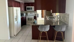 A kitchen with a refrigerator, microwave, oven, and bar stools. - Tropical Paradise with gulf access and heated pool (Cape Coral)