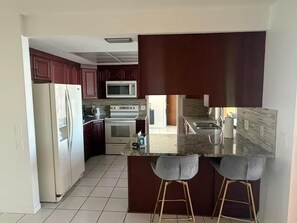 A kitchen with a refrigerator, microwave, oven, and bar stools. - Tropical Paradise with gulf access and heated pool (Cape Coral)