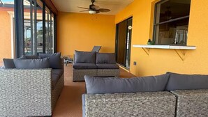 A sunlit patio with wicker furniture, a ceiling fan, and a window overlooking a garden. - Tropical Paradise with gulf access and heated pool (Cape Coral)