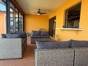 A sunlit patio with wicker furniture, a ceiling fan, and a window overlooking a garden. - Tropical Paradise with gulf access and heated pool (Cape Coral)
