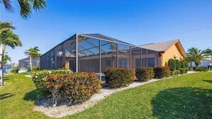 A modern house with a glass-enclosed porch, a well-maintained lawn, and a clear blue sky. - Tropical Paradise with gulf access and heated pool (Cape Coral)