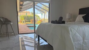 A bedroom with a bed, a chair, a lamp, and a view of a pool and outdoor area. - Tropical Paradise with gulf access and heated pool (Cape Coral)
