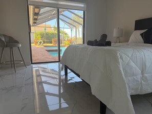 A bedroom with a bed, a chair, a lamp, and a view of a pool and outdoor area. - Tropical Paradise with gulf access and heated pool (Cape Coral)