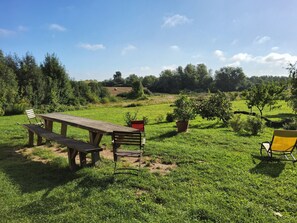 A picnic table with benches and chairs in a grassy field with trees in the background. - Vrbo Property (Nordwestuckermark)