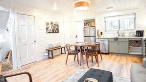 Tilava olohuone, jossa on korkea katto, puupalkit, ruokapöytä sekä modernilla kalustuksella varustettu keittiö.
