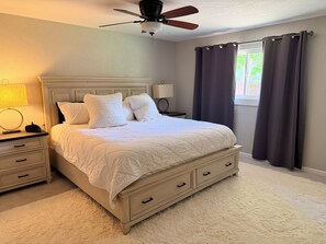 Quarto com cama, mesas de cabeceira, ventilador de teto, janela com cortinas e abajur.