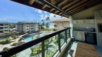 A balcony with a view of a pool, palm trees, and a building with a tiled roof.