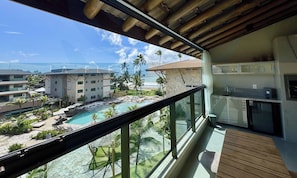 Un balcón con vista a una piscina, palmeras y un edificio con techo de tejas.