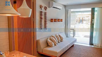 Uma sala de estar moderna com um sofá, uma mesa com copos, um lustre pendente e um ar condicionado fixado na parede.