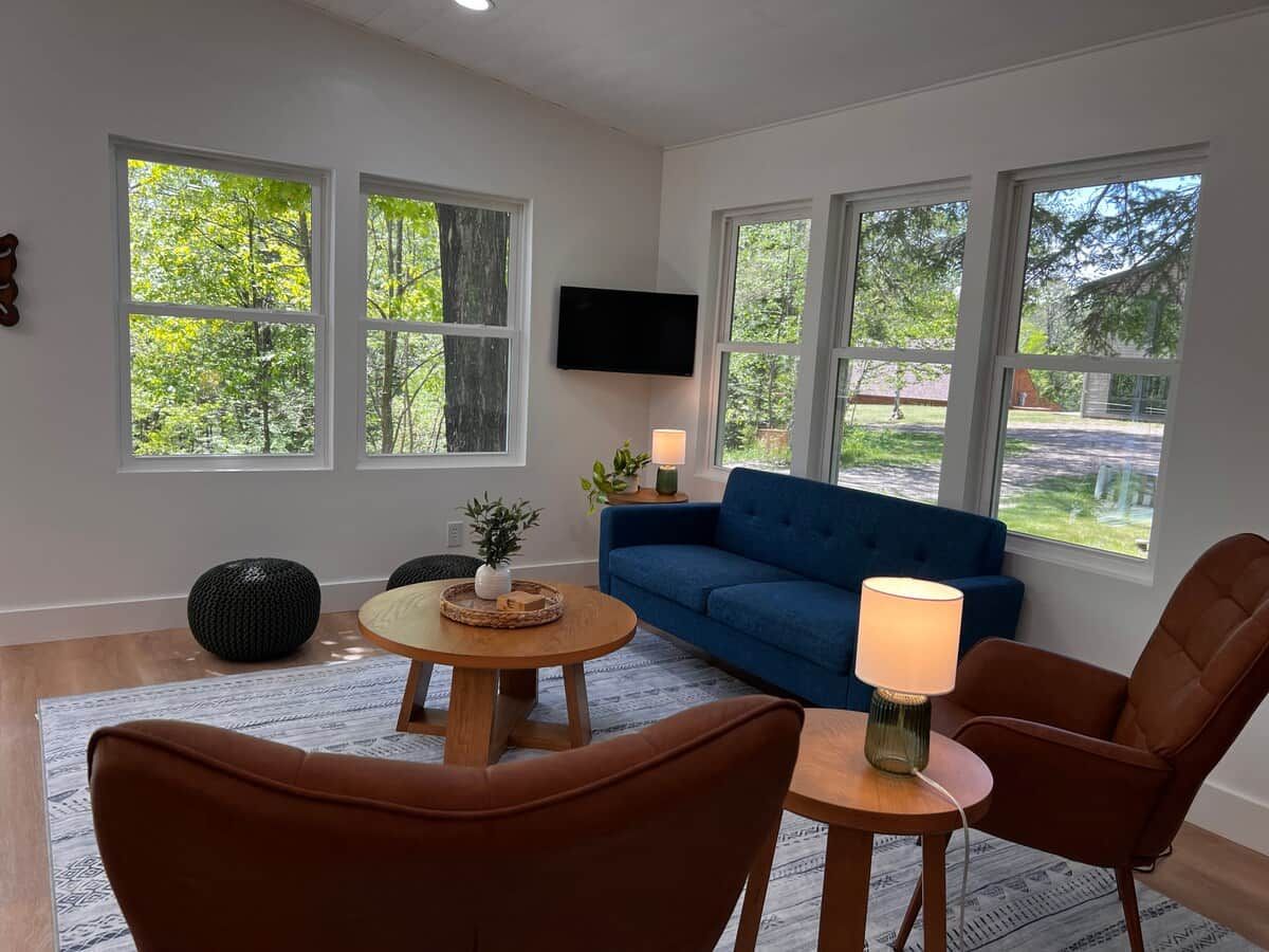 A living room with a blue sofa, two brown chairs, a coffee table, and a TV mounted on the wall.
