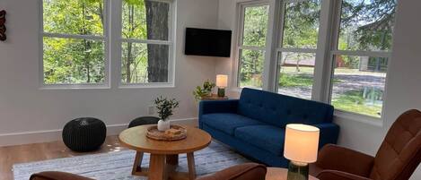 A living room with a blue sofa, two brown chairs, a coffee table, and a TV mounted on the wall.