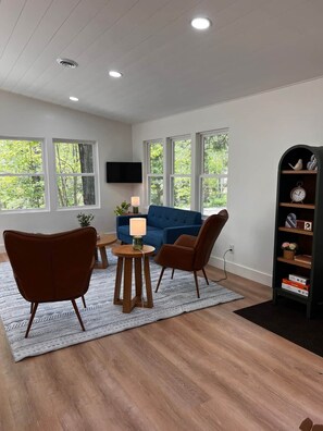 A modern living room with a blue sofa, two brown armchairs, a wooden coffee table, and a bookshelf.