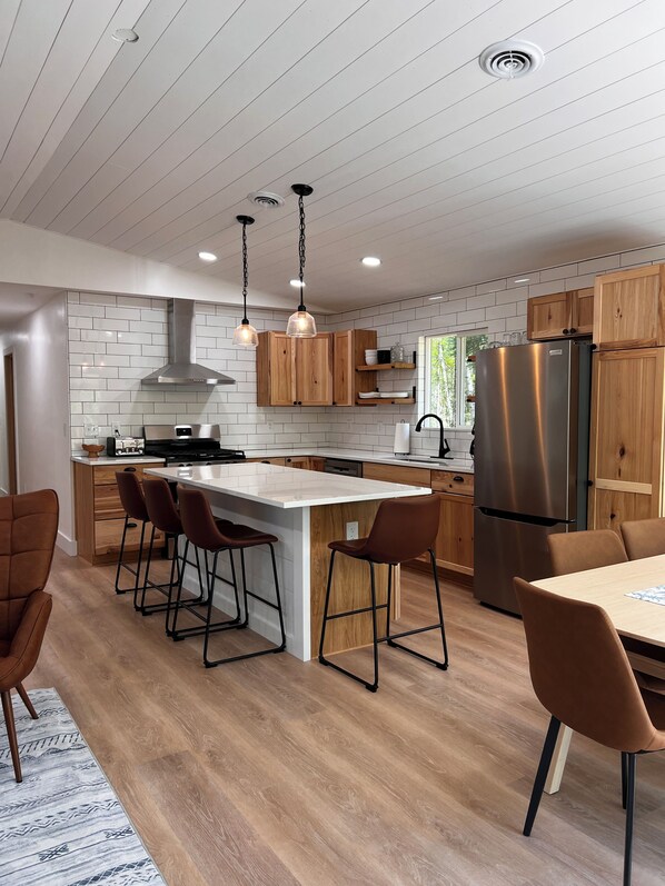 A modern kitchen with a central island, wooden cabinets, and pendant lighting.