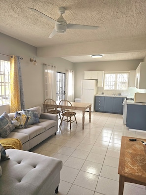A living room with a sofa, chairs, a dining table, a kitchen area with cabinets and appliances, and a ceiling fan. - Fabulous 1-bedroom sea view apartment with AC in charming Basseterre (Basseterre)