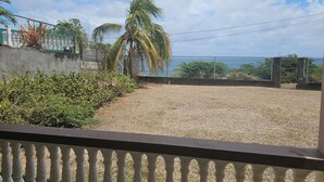 Vista de varanda com área de cascalho, uma palmeira e um cercado.
