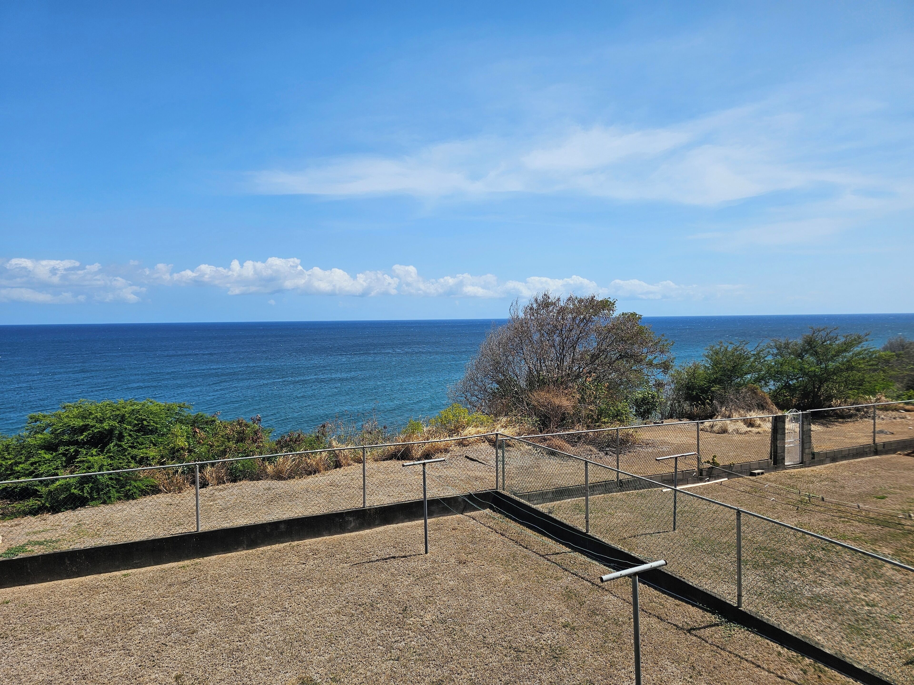 A coastal view with a clear sky, a fenced area, and a tree.. Fabulous 1-bedroom sea view apartment with AC in charming Basseterre