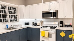 Uma cozinha moderna com armários brancos, fogão a gás, micro-ondas e cafeteira.