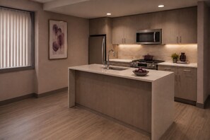 A modern kitchen with a central island, stainless steel appliances, and a minimalist design. - The Ravona Suites (Toronto)