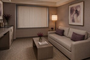 A modern hotel room with a sofa, a coffee table with a vase, a lamp, and a painting on the wall. - The Ravona Suites (Toronto)